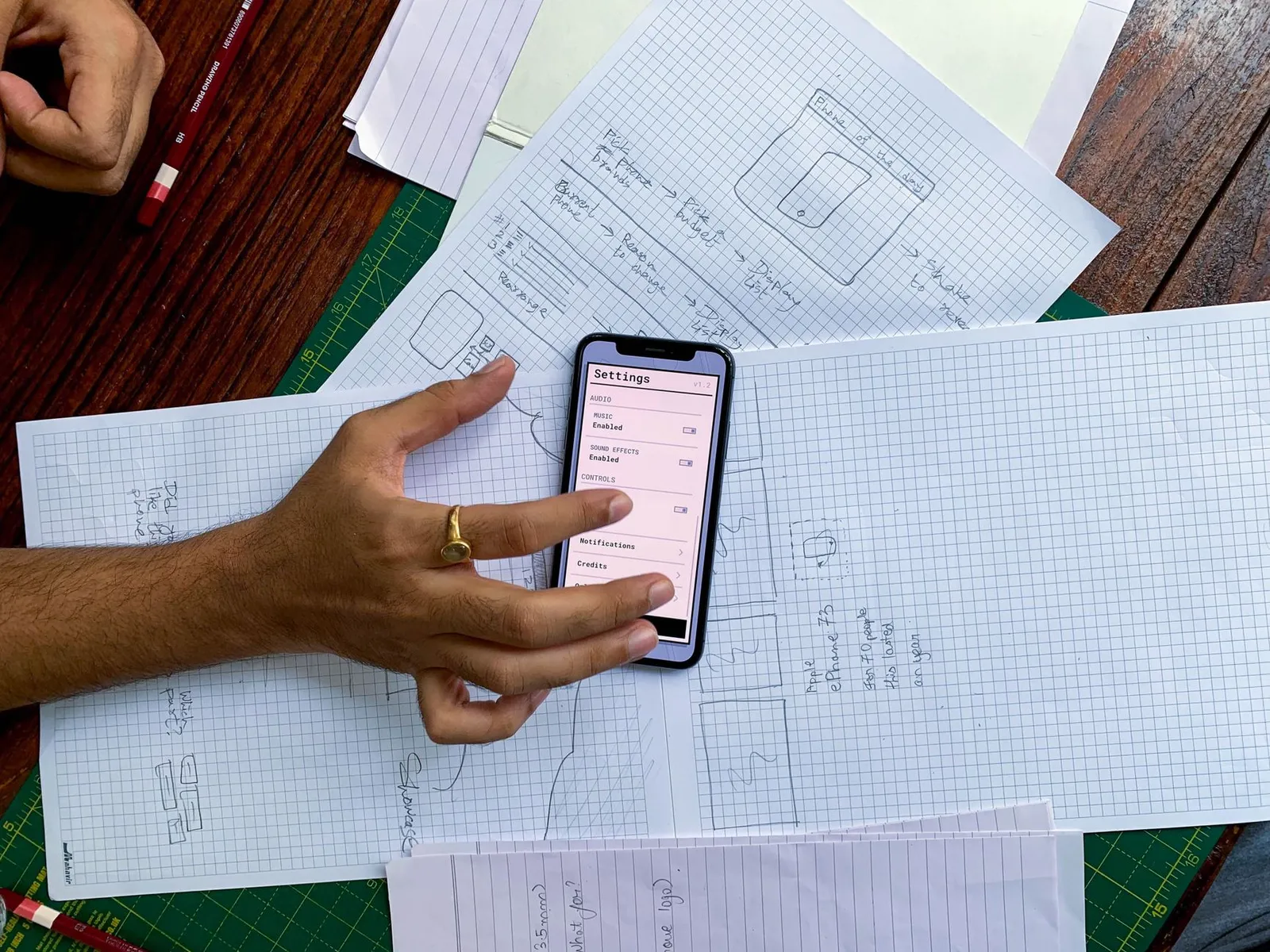 App developer in Jashore holding a phone over paper sketches of app screens while planning a local business app