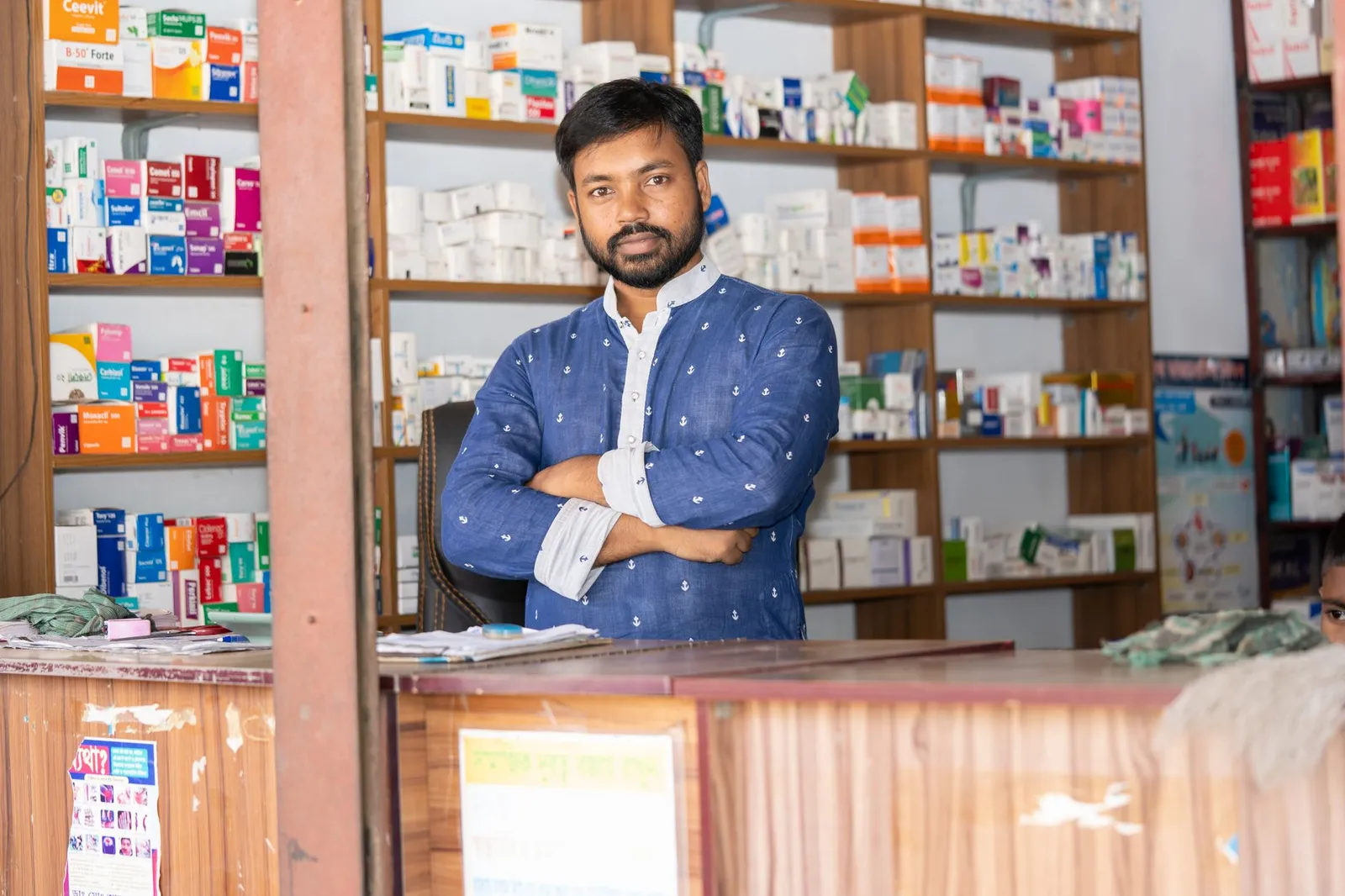 Pharmacy owner standing behind his shop counter in Bangladesh — the kind of local business that usually runs on a Facebook page alone
