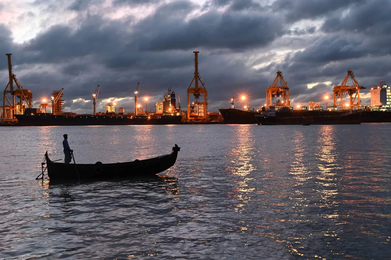 Cranes and ships at Chattogram port at twilight, with a fisherman's boat in front — the port businesses a remote app developer in Chattogram builds apps for