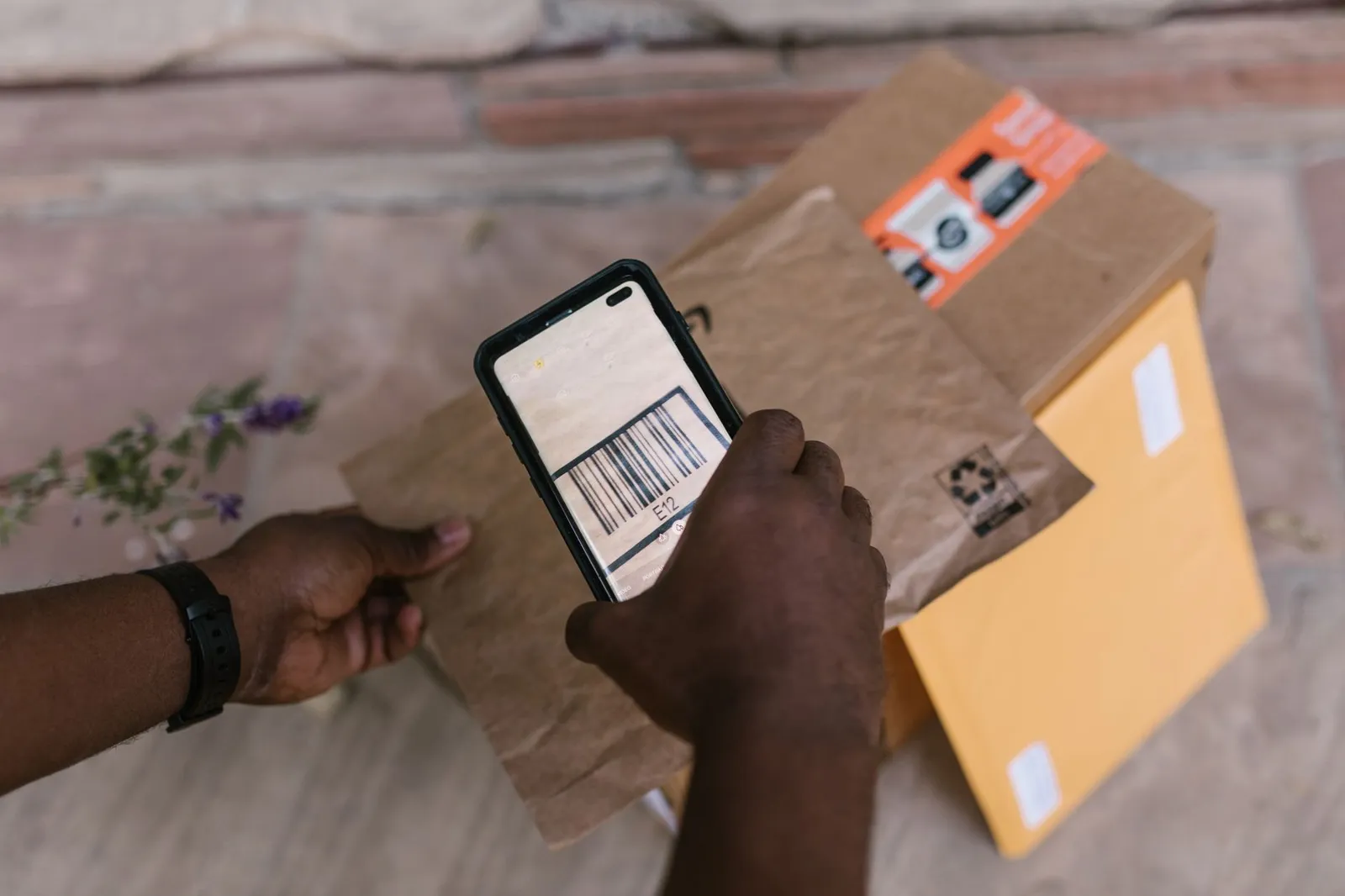 Hands scanning a parcel's barcode with a smartphone — the kind of shipment status an app can show customers without a phone call
