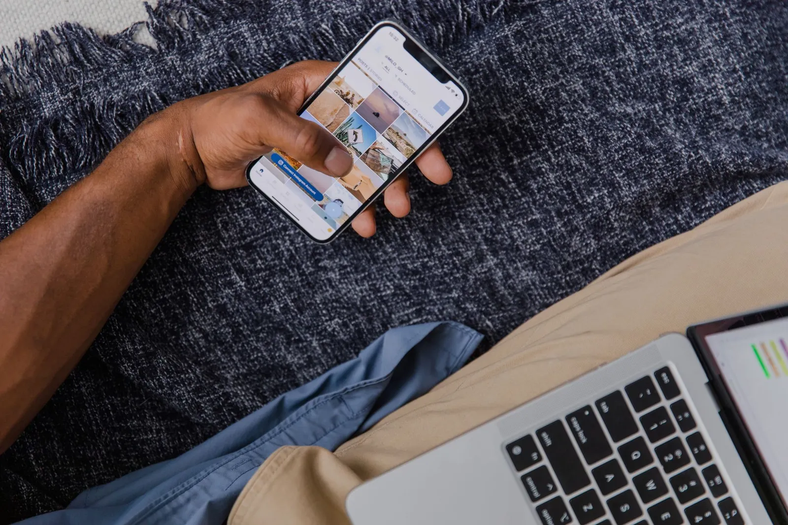 Hand holding a smartphone with a shopping app open beside a laptop — the repeat customer an app is built for