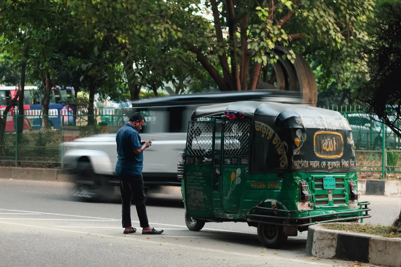 Man checking his phone beside a CNG auto-rickshaw on a busy Dhaka road — searches like his happen all day across the city