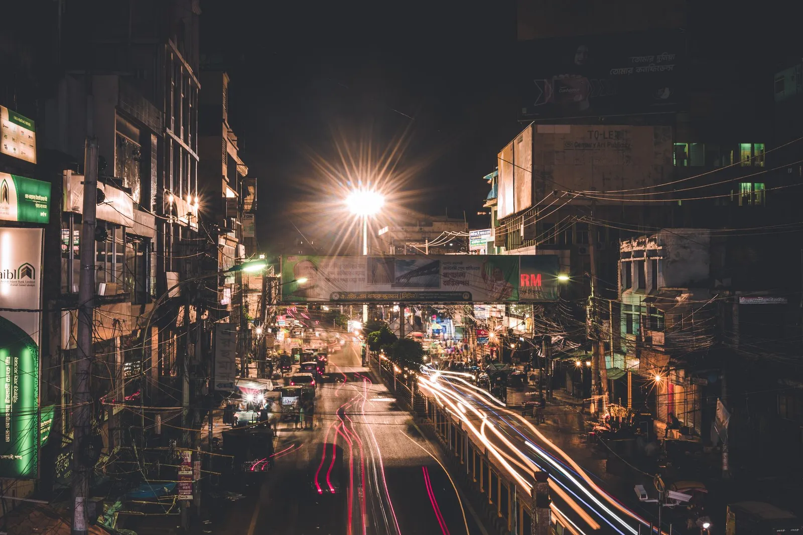 Long-exposure view of a busy Rajshahi city street at night, lit shop signs and traffic trails — the city an app developer in Rajshahi builds for