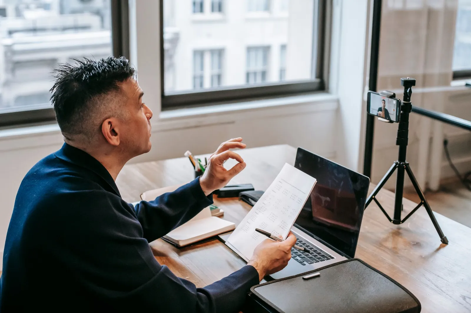 Man on a video call with a laptop and a phone on a tripod, reviewing notes — how a remote website project is discussed