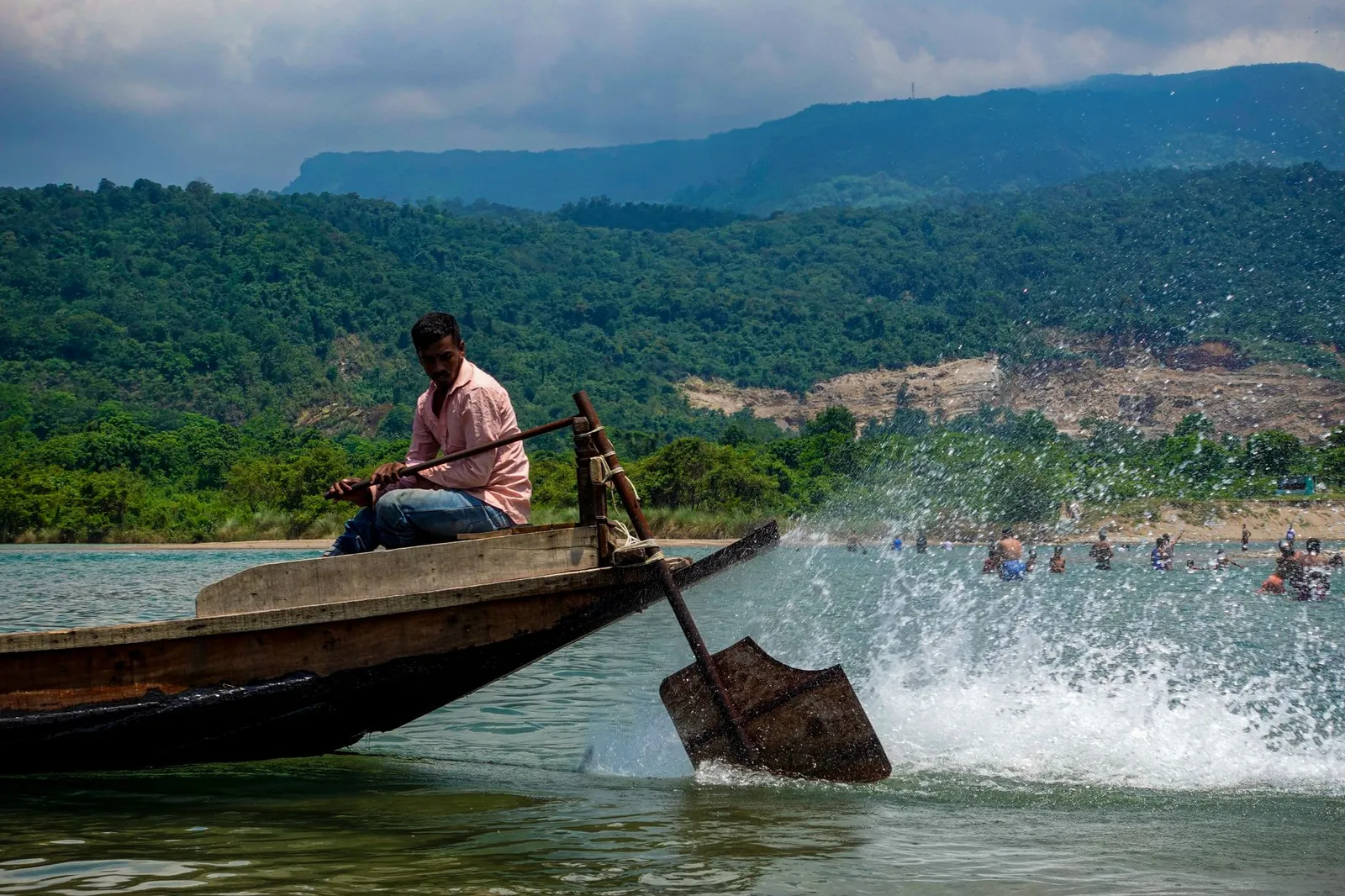 Boatman steering a wooden boat on a river below green hills in Sylhet — the division an app developer in Sylhet builds booking and ordering apps for