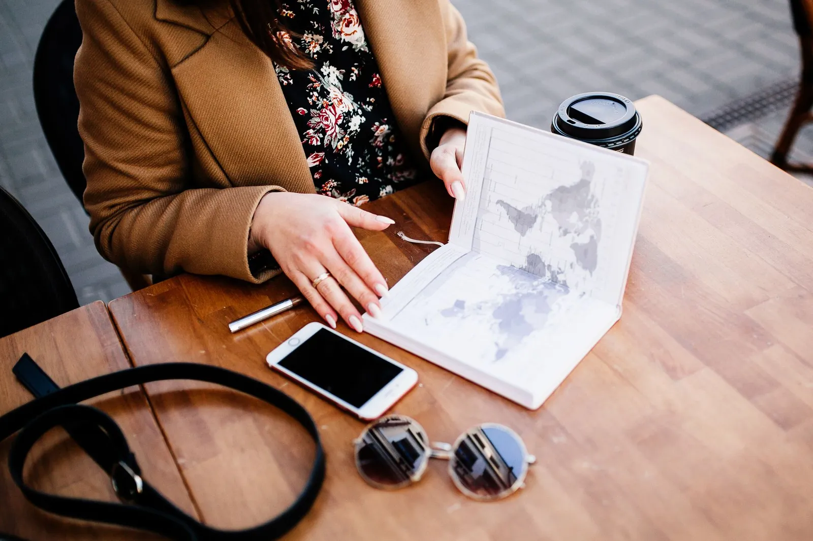 Traveller planning a trip with a map, a coffee, and a smartphone on a wooden table — the moment a booking app gets opened